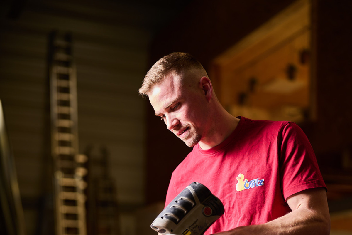 Sebastian Henn trägt ein rotes T-Shirt mit fritz-Logo und hält eine schwarze, handliche Maschine.