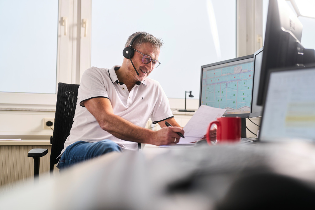 Mitarbeiter von Fritz spricht am Headset und hält einen Bauplan in den Händen