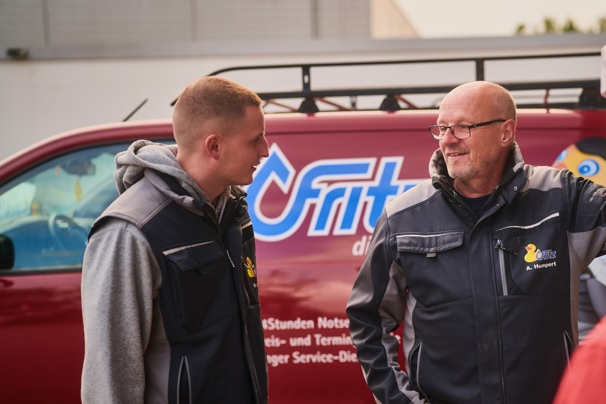 Zwei Kollegen unterhalten sich draußen vor einem Serviceauto von Fritz.