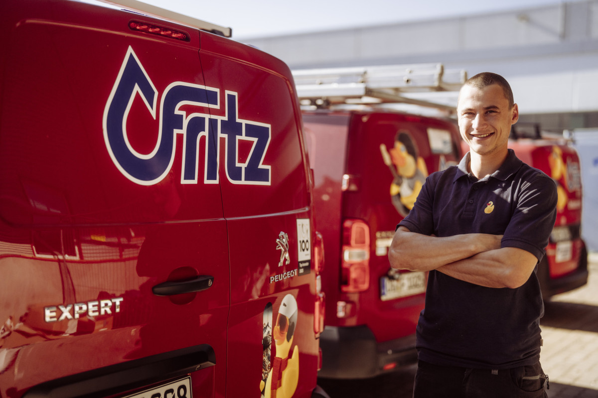 Gregor steht mit verschränkten Armen und lächelnd neben einem Firmenfahrzeug von Fritz.